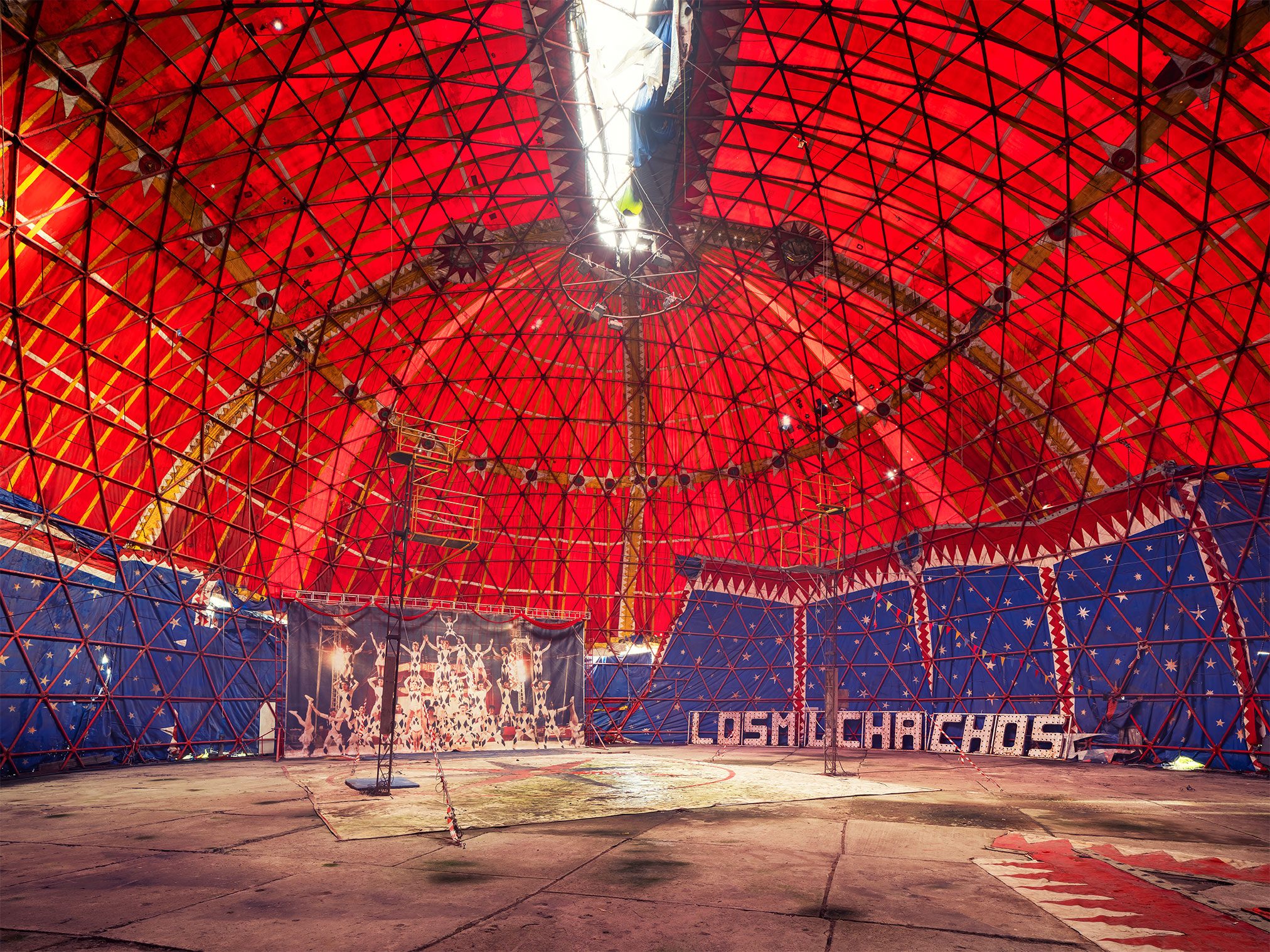 Interior of a derelict circus tent with red and blue canvas and an illuminated sign in Spain