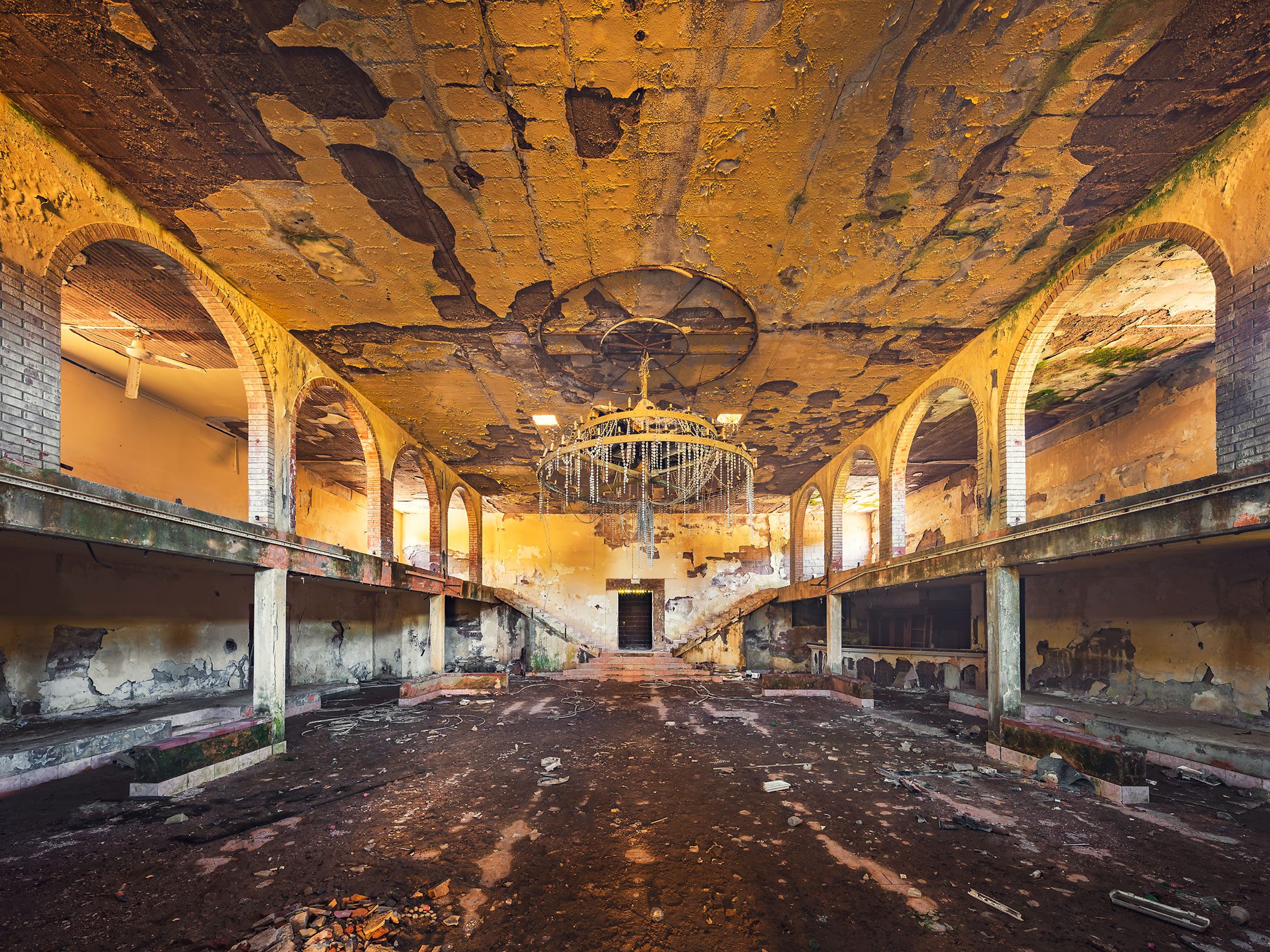 Decaying hall with arched alcoves and a chandelier in an old discotheque in Italy