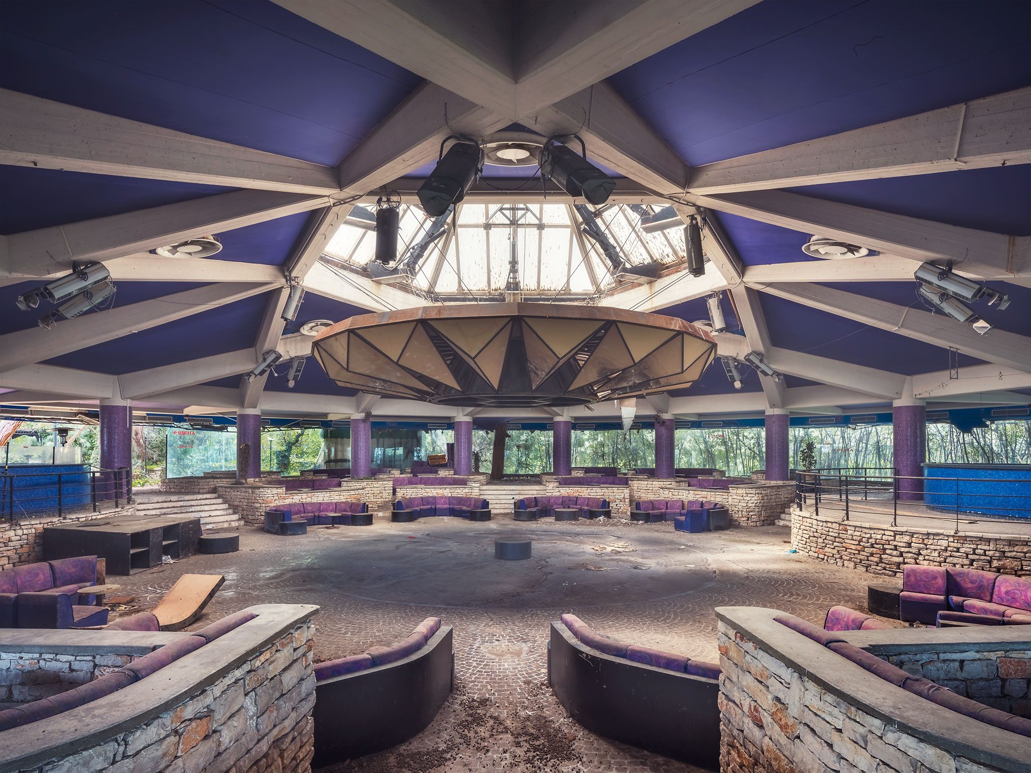Circular dance floor with purple seating alcoves beneath a geometric roof in a disused discotheque in Italy