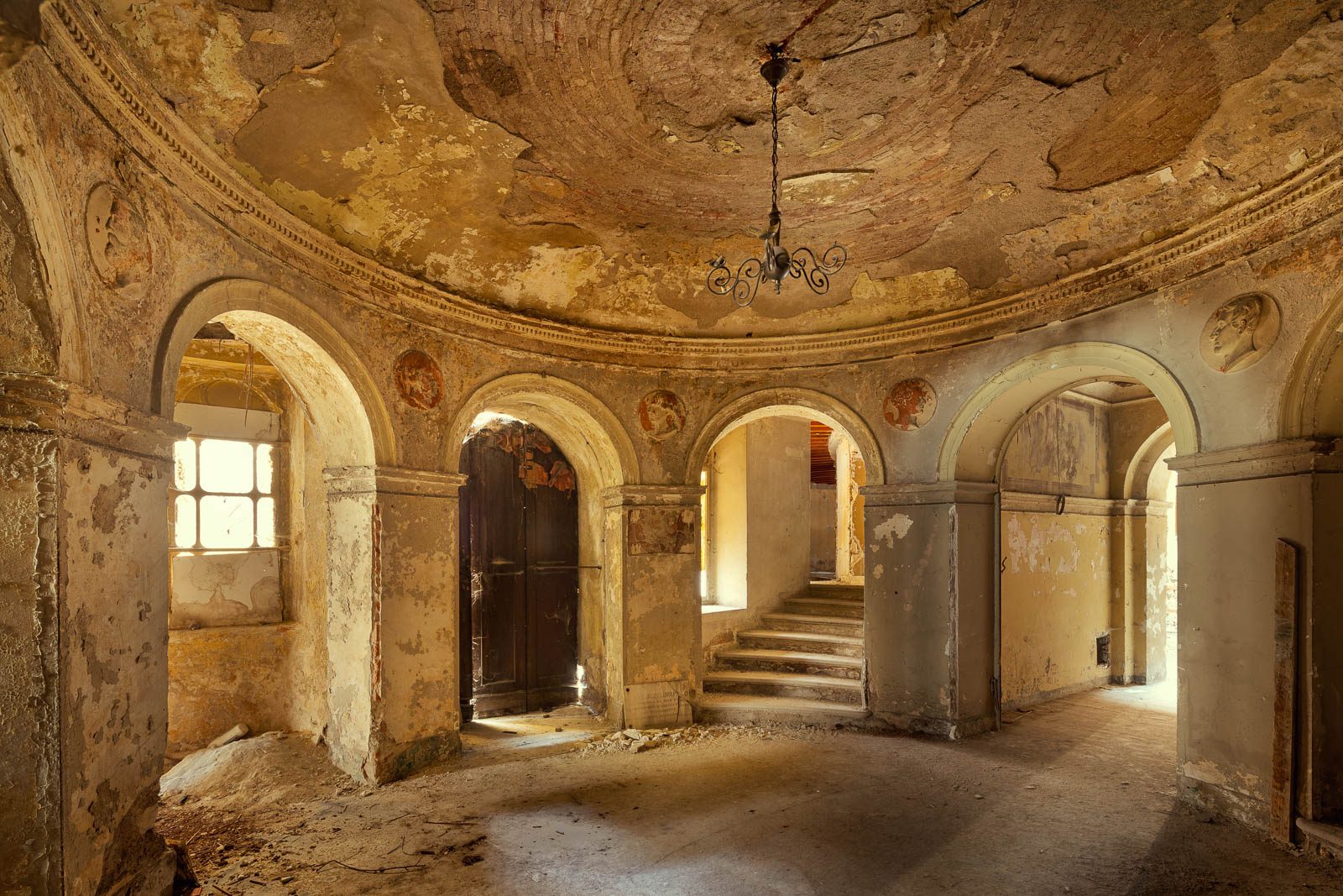 Round room with several arched doorways and painted wall medallions in a historic theatre in Italy