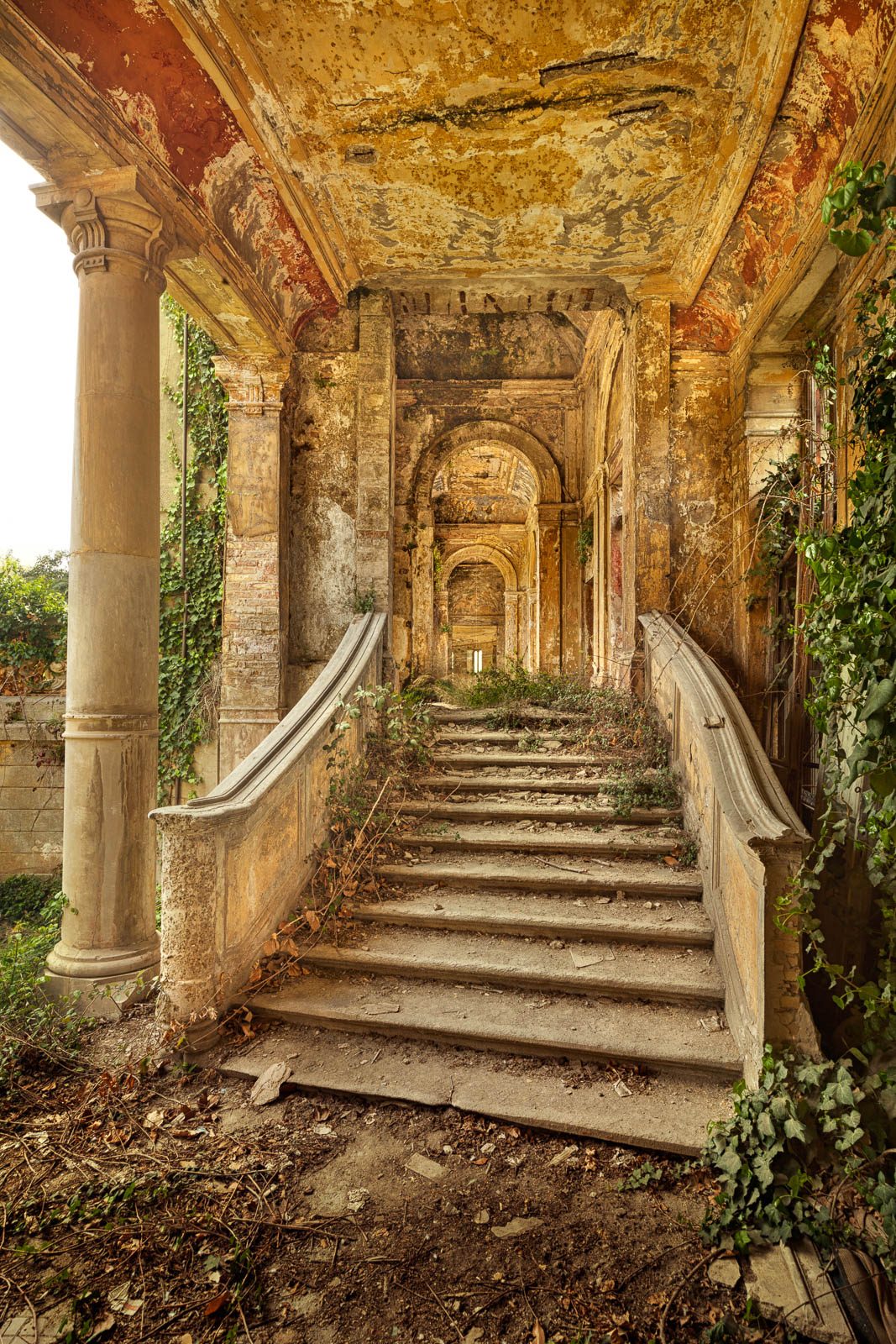 Ivy-covered outdoor staircase between columns in a derelict spa building in Italy