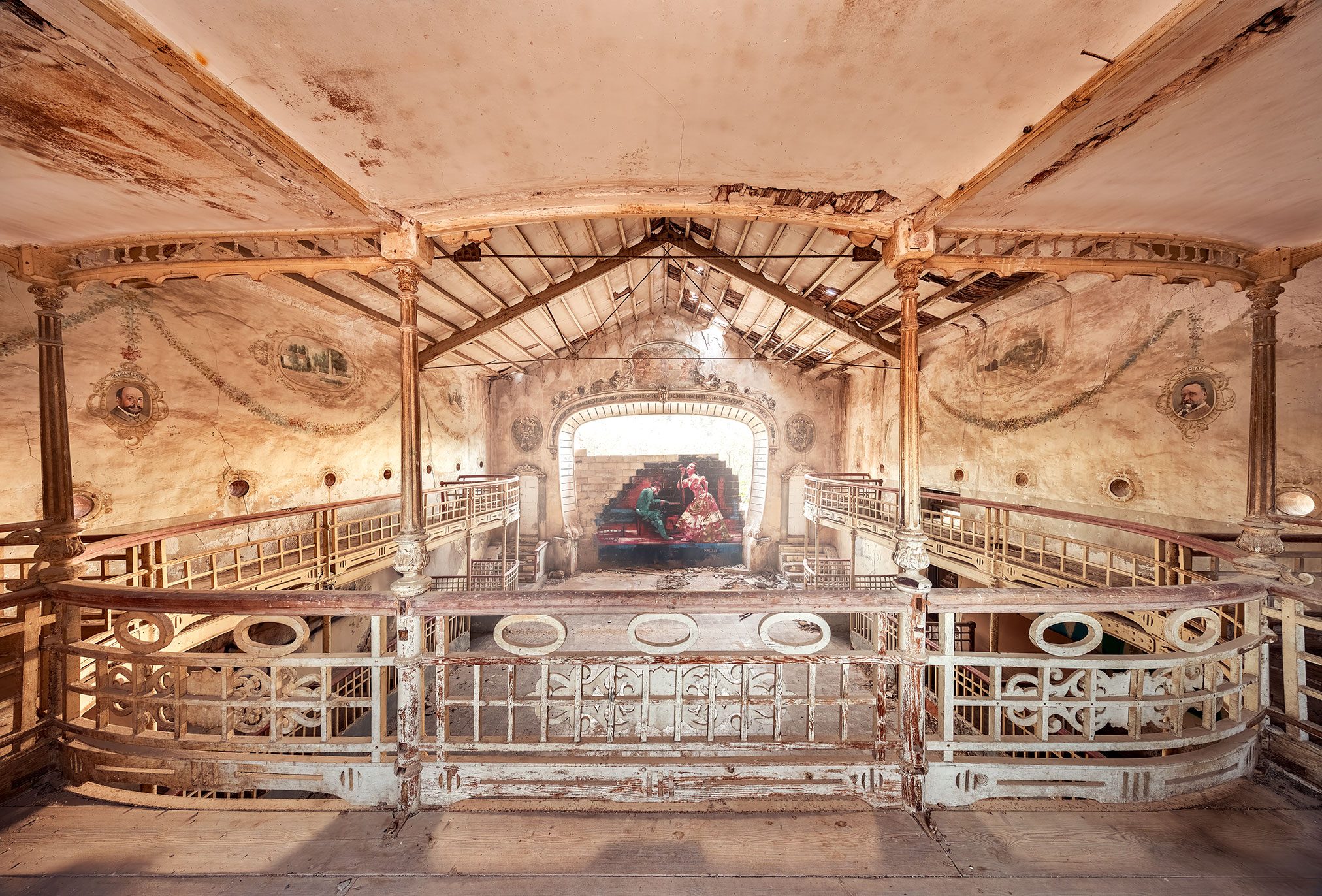 Theatre hall with wooden roof structure and an illuminated stage with a wall painting in Spain