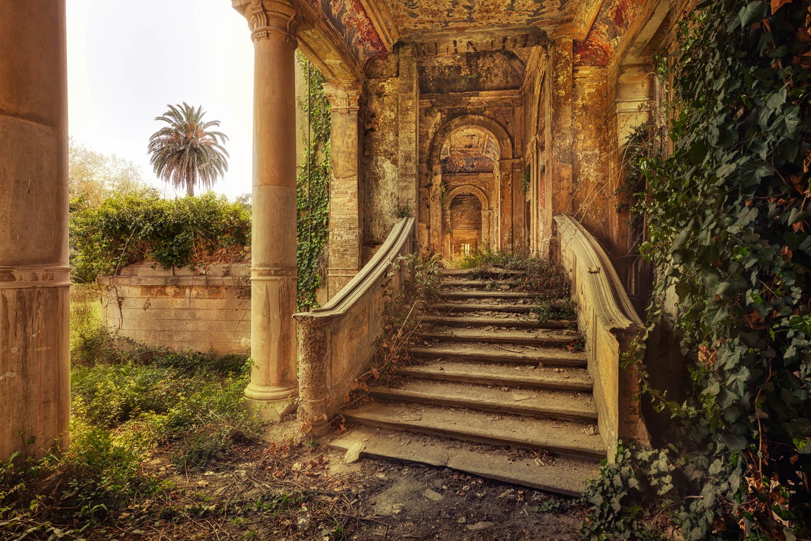Colonnade with an outdoor staircase and a palm tree in front of a derelict spa building in Italy