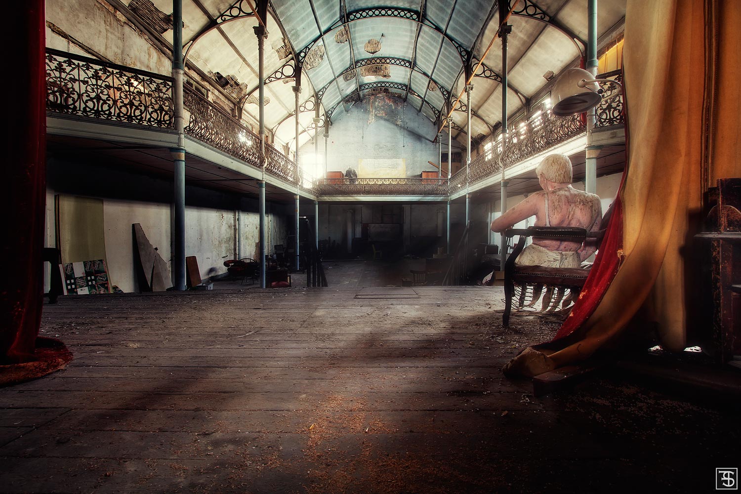 Industrial-looking hall with a glass roof, gallery, and a seated figure in a derelict theatre in Belgium