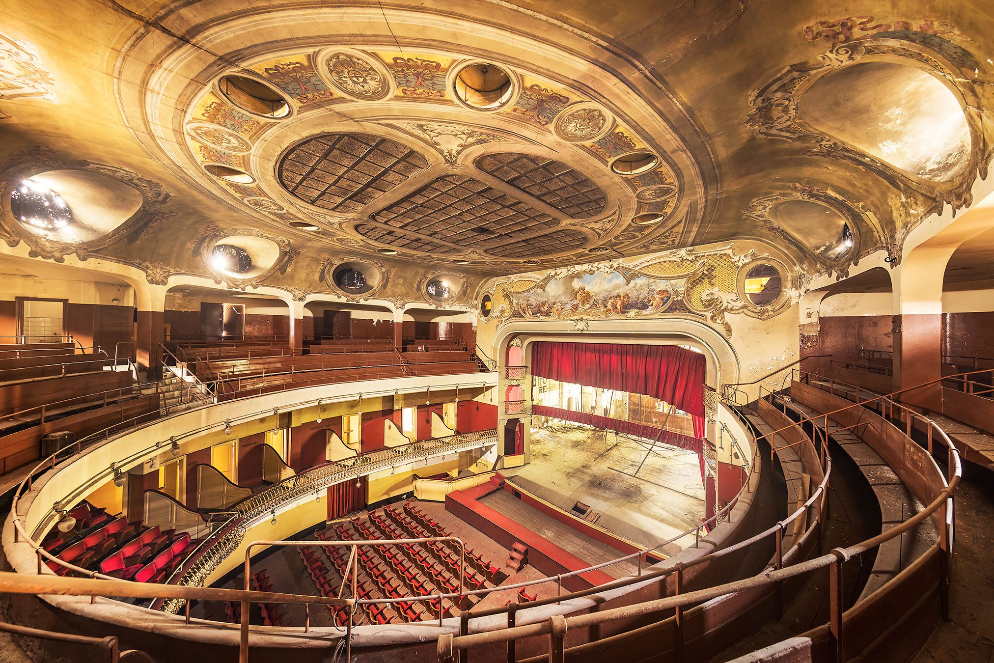 Horseshoe-shaped auditorium with gilded ceiling painting and red curtain in a historic theatre in Italy