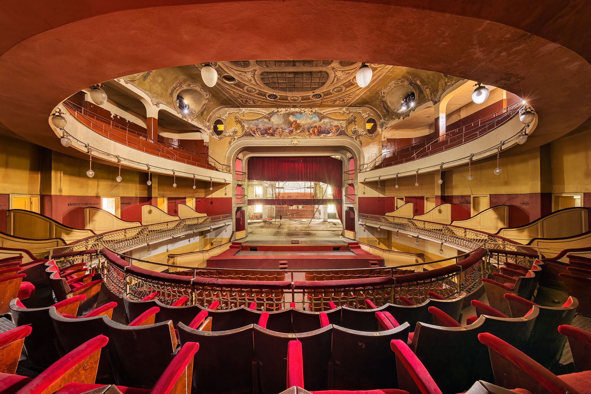 Rows of red seats and a small stage beneath a vaulted ceiling in a historic theatre in Italy