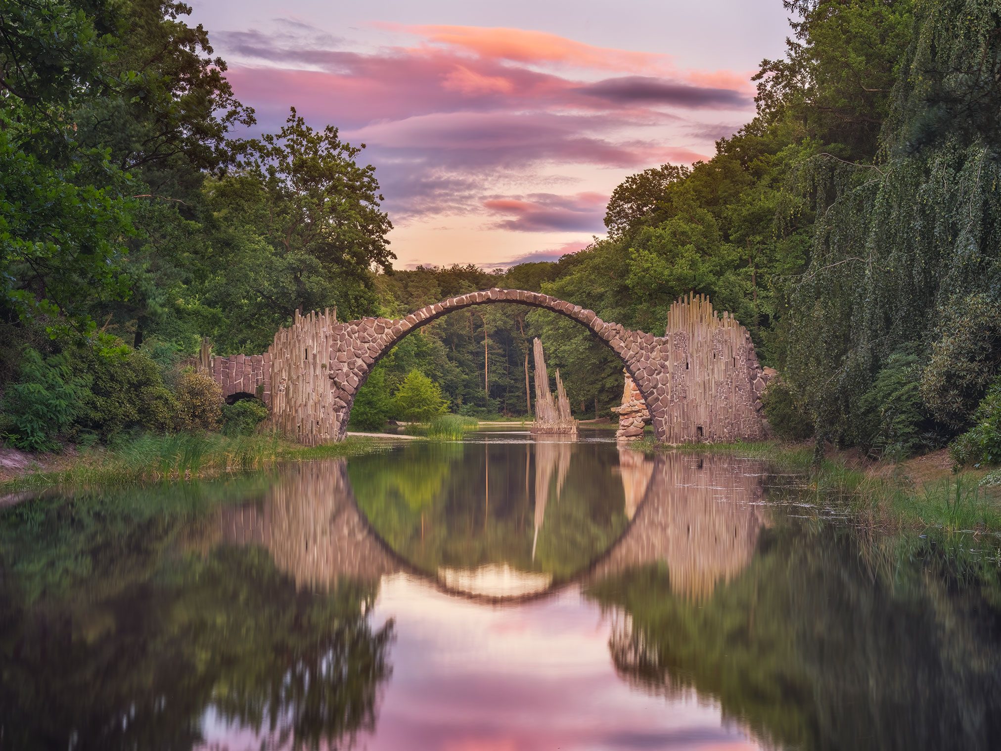 Steinerne Bogenbrücke mit Kreisspiegelung über einem See in Deutschland