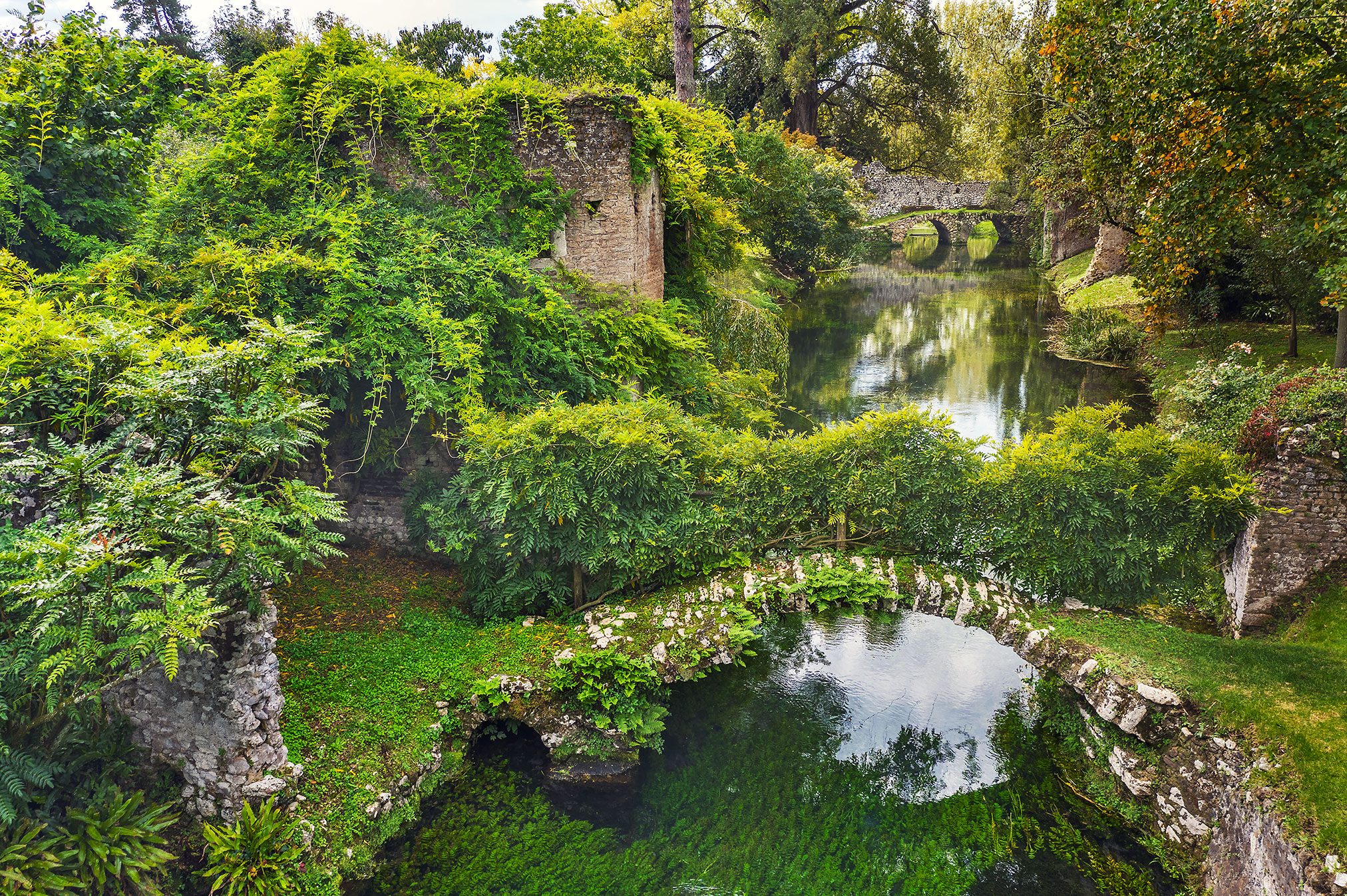 Efeuüberwachsener Ruinenturm mit Steinbrücke an einem Kanal in Italien