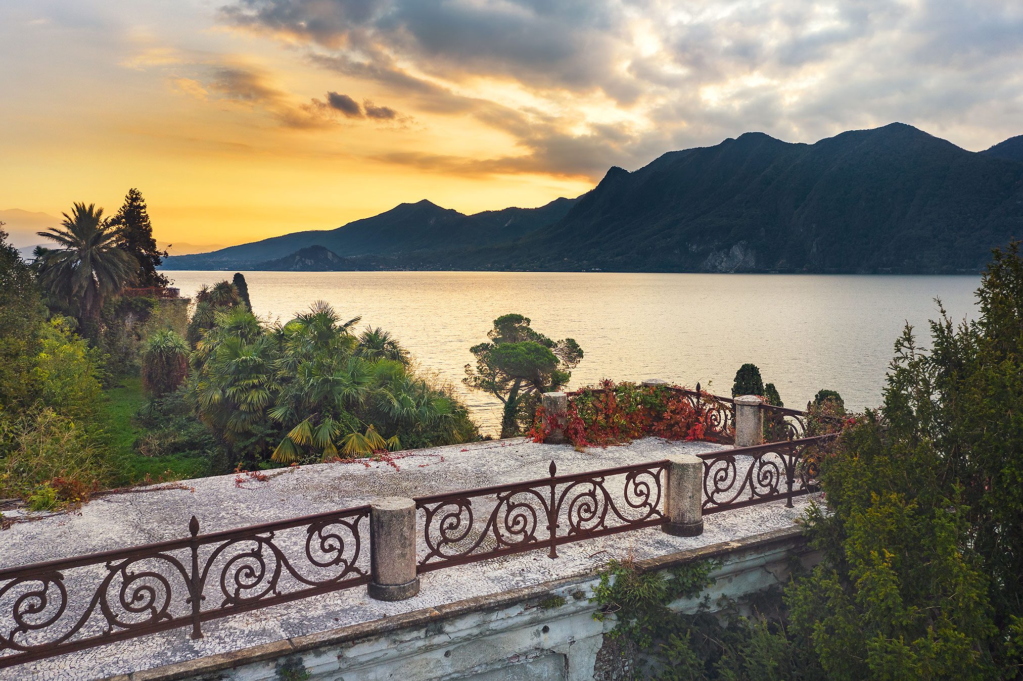Terrasse mit schmiedeeisernem Geländer über einem See bei Sonnenuntergang in Italien