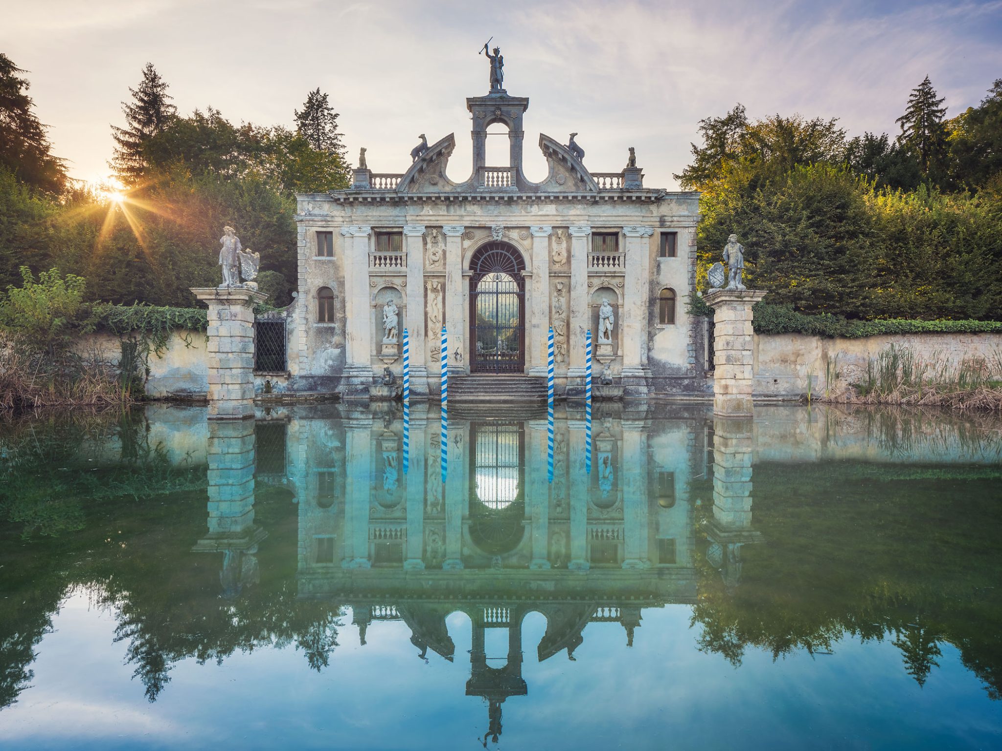 Barockes Gartentor mit Statue und Spiegelung in einem Wassergraben in Italien