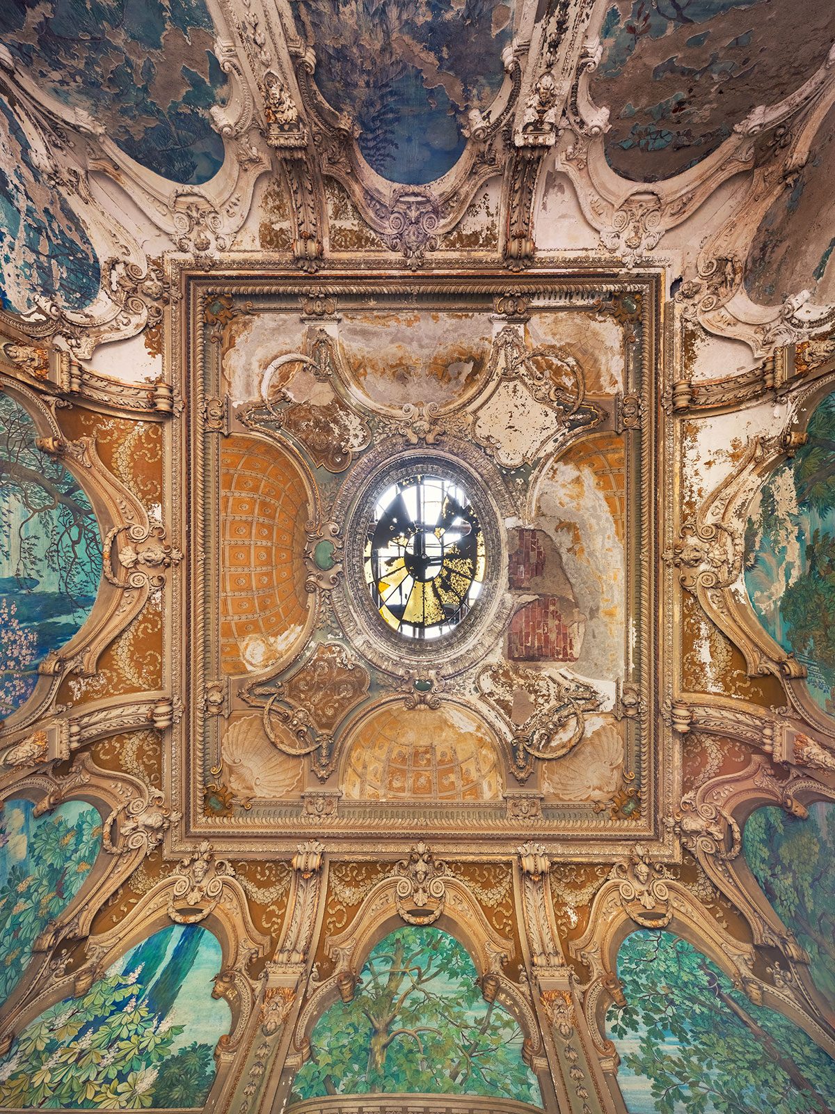 A richly decorated ceiling dome with an oval window in an abandoned palazzo in Italy