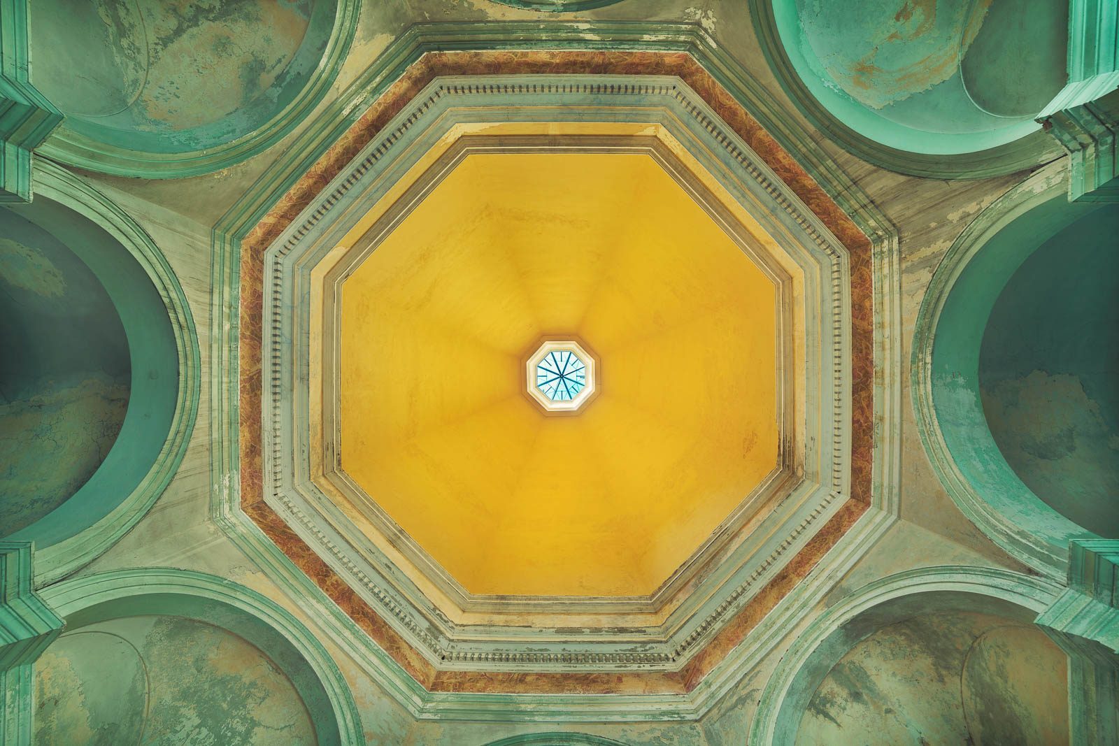 An octagonal dome in yellow tones with a small skylight in an abandoned hospital in Italy