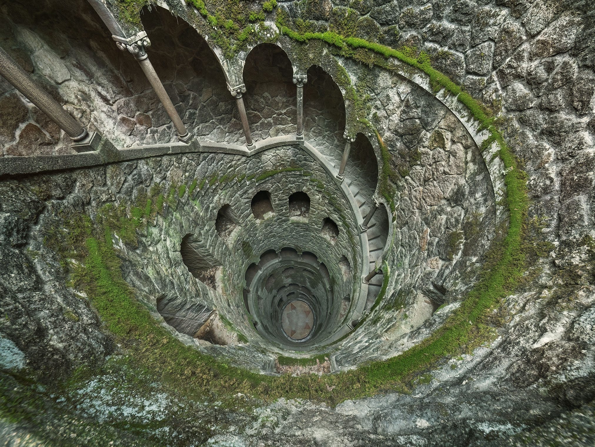 Moss-covered spiral well with a staircase in a historic park in Portugal