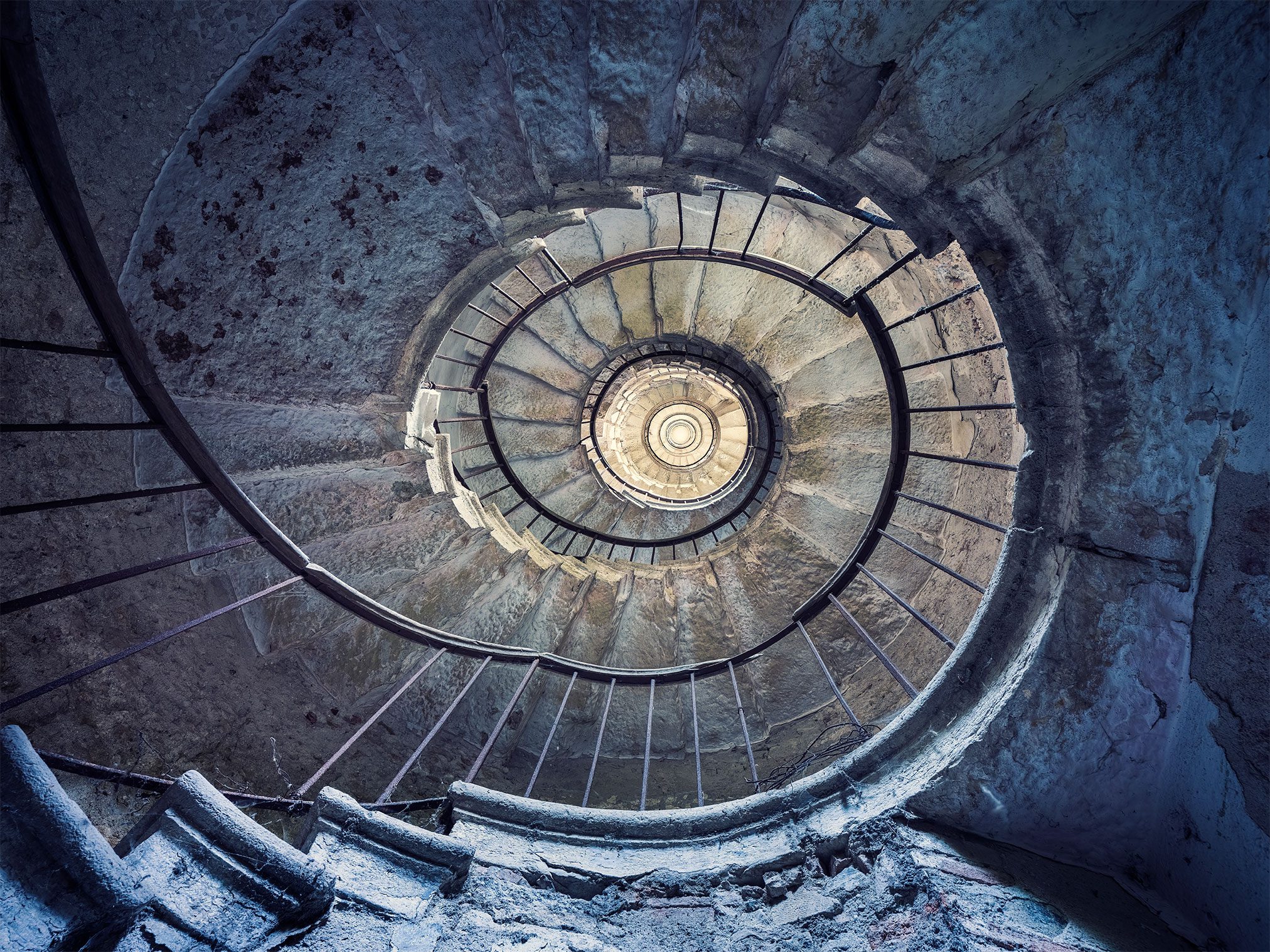 A stone spiral staircase in cool blue tones inside an abandoned villa in Italy