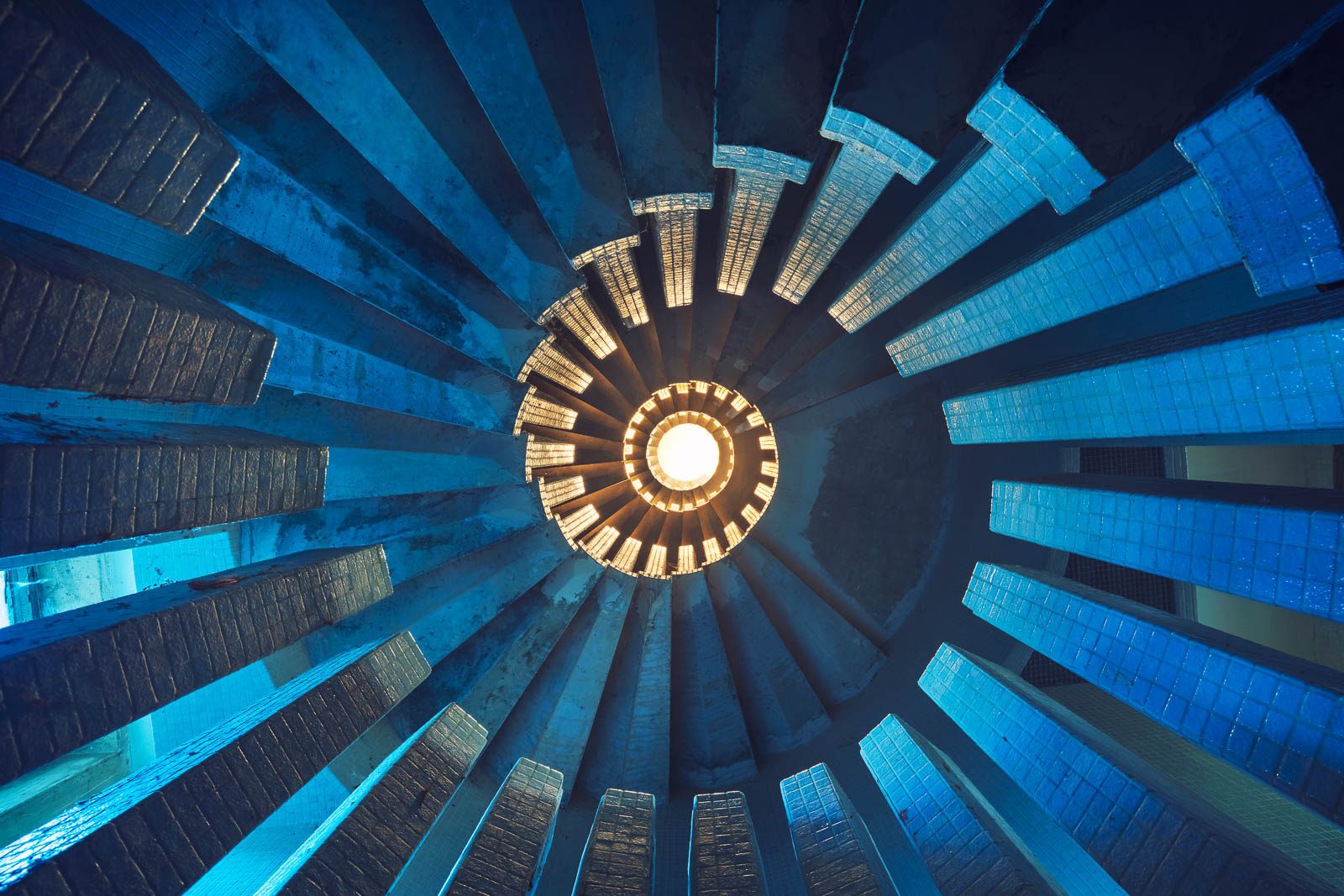 A blue-lit spiral staircase of concrete and glass blocks in an abandoned château in France