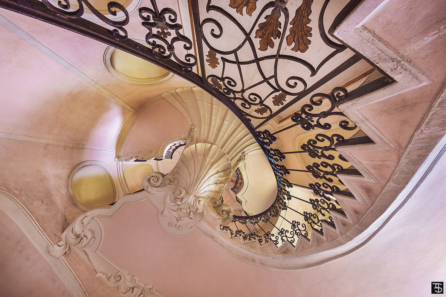 A stucco-decorated spiral staircase with a wrought-iron railing inside an abandoned villa in Italy