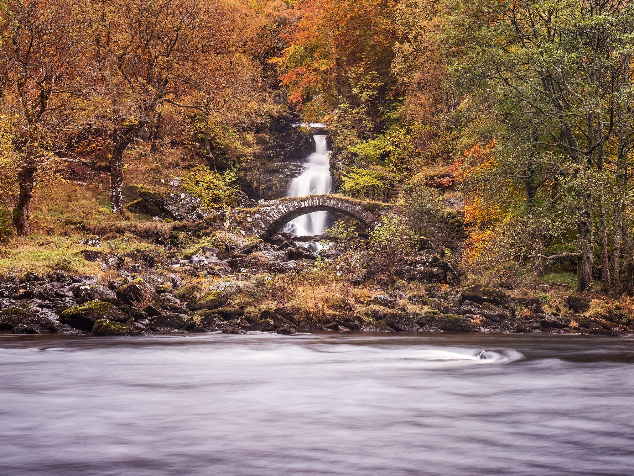 Steinbrücke an einem Wasserfall über einem Fluss, Schottland