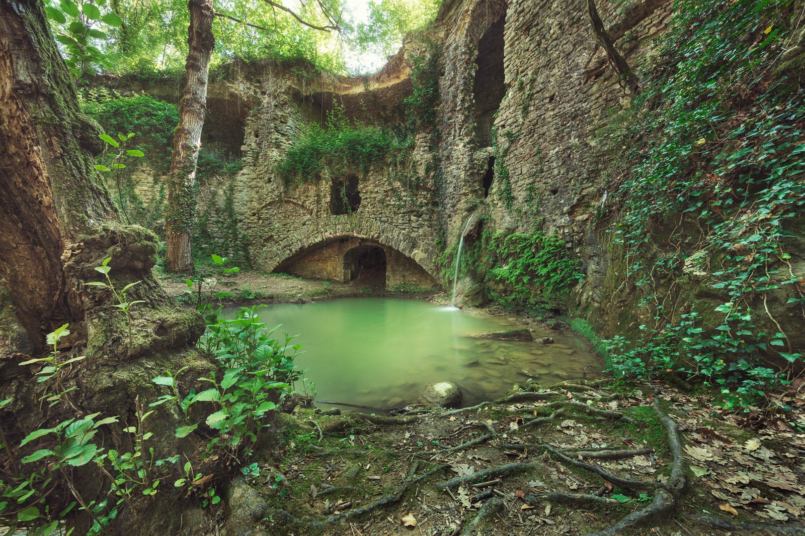 Ruin with a waterfall above a green pool, Tuscany, Italy