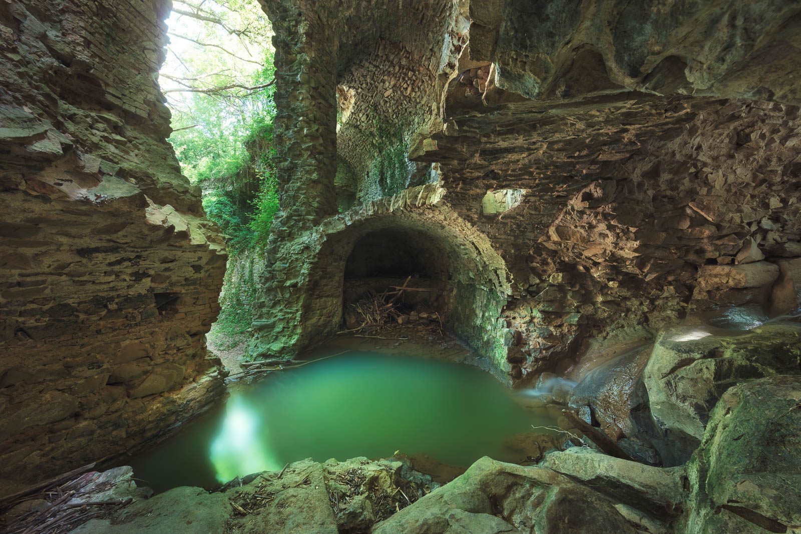 Vaulted mill ruin above a green pool of water, Tuscany, Italy