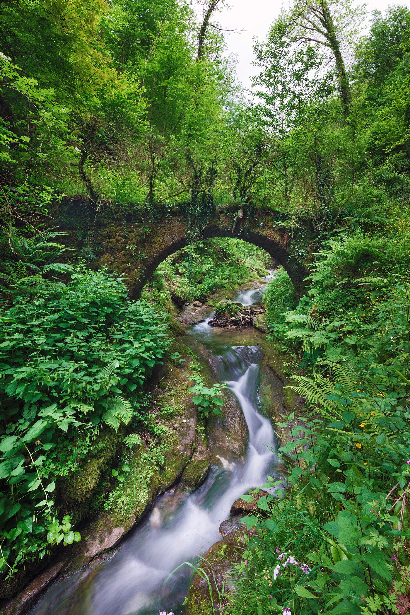 Moosbewachsener Steinbogen über einem Bach, Toskana, Italien